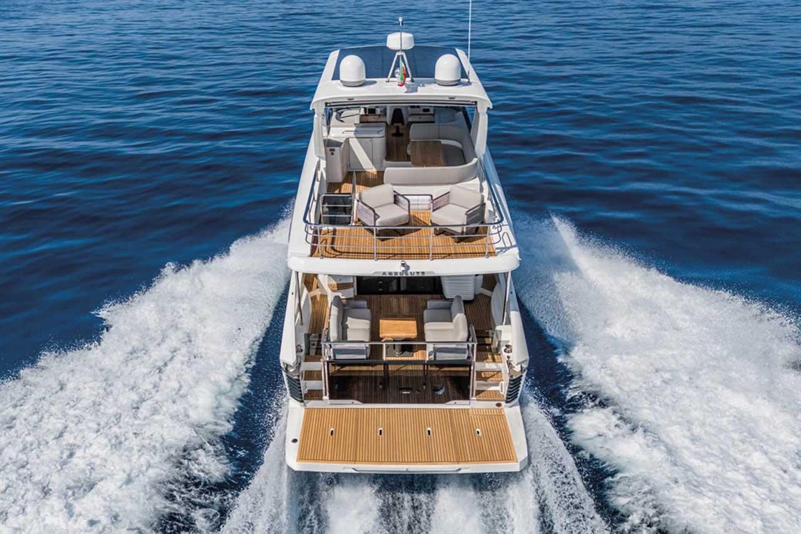 A luxury yacht with a spacious deck and seating, cruising through calm blue waters, leaving a wake behind.